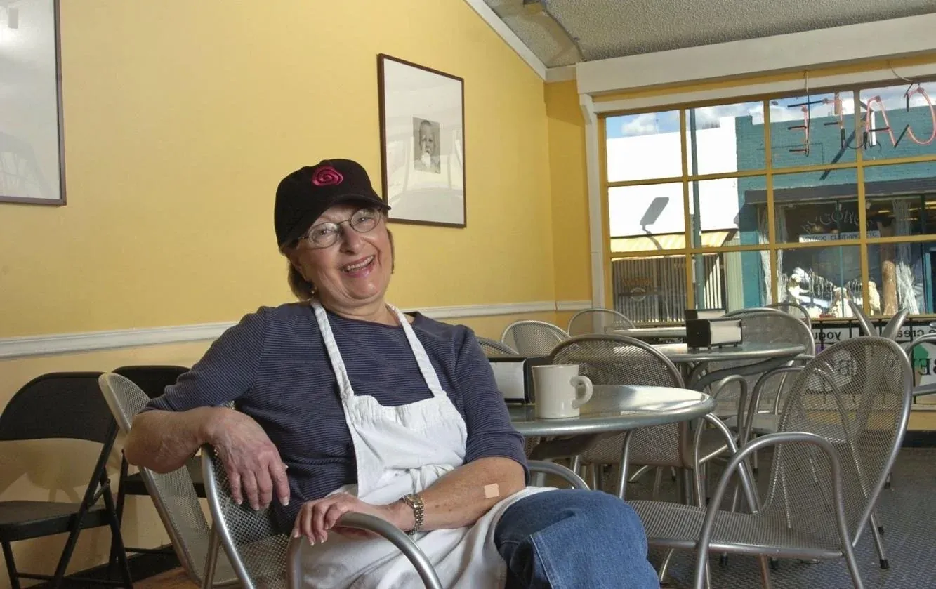 Bev, in a cap and apron, smiling at a table in her West Cary Street shop