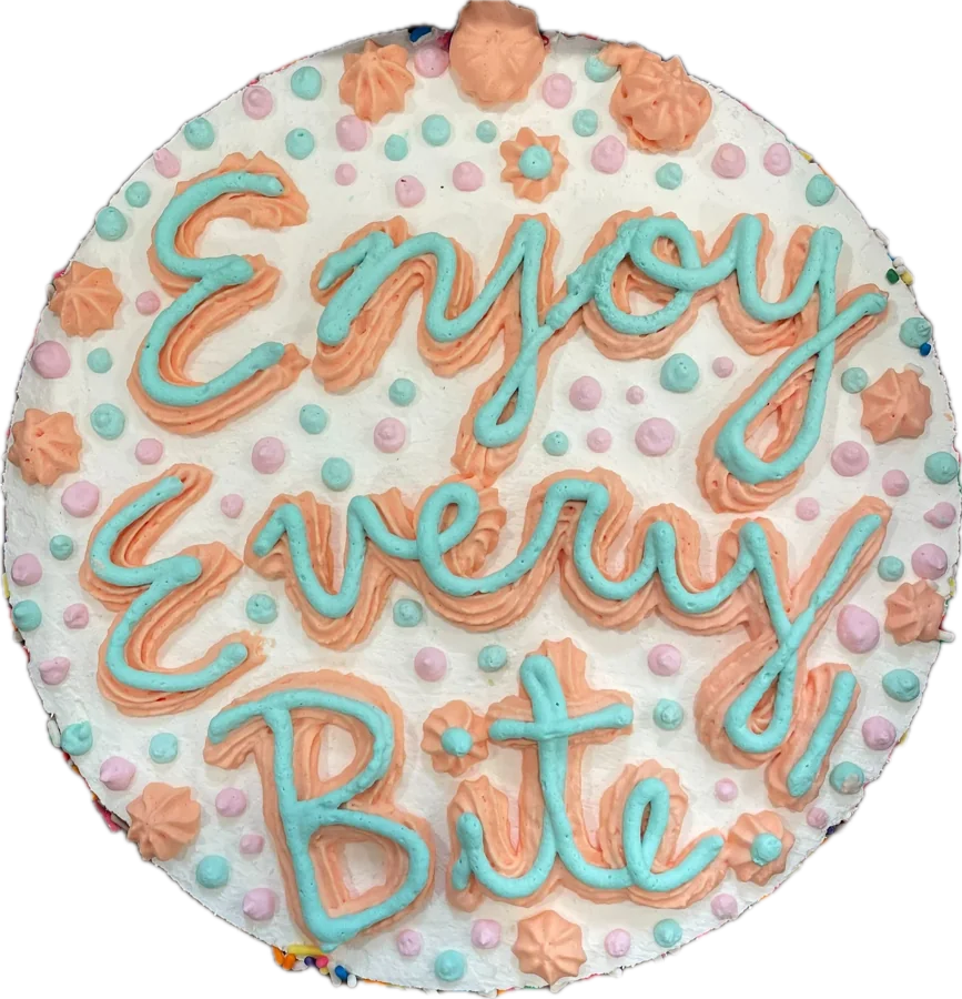 Ice cream cake piped with “Enjoy Every Bite” in blue, with pink rosettes and pastel dots