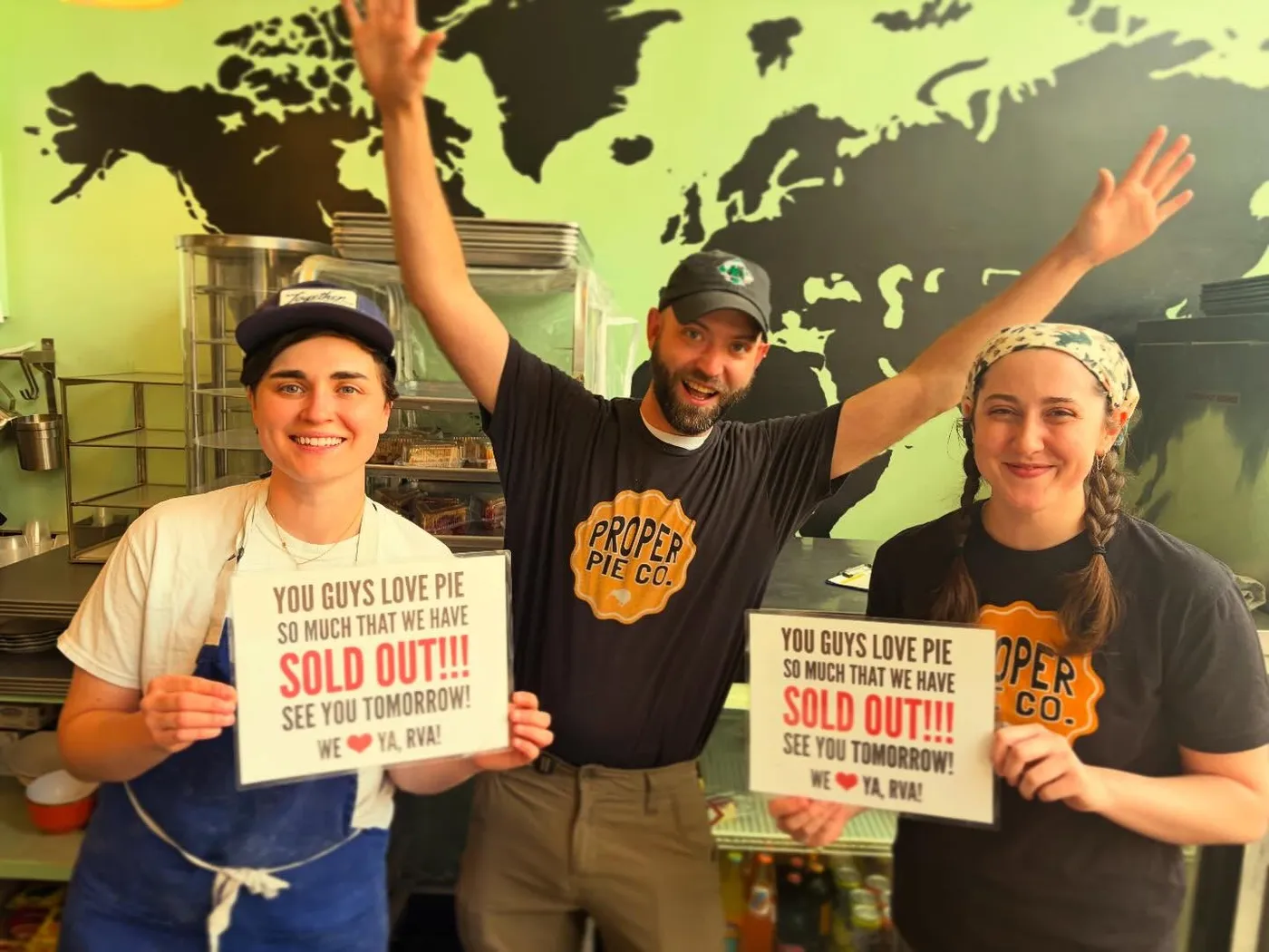 Three of the Proper Pie crew in the kitchen, arms up, holding signs that read “You guys love pie so much that we have sold out!!! See you tomorrow! We love ya, RVA!”