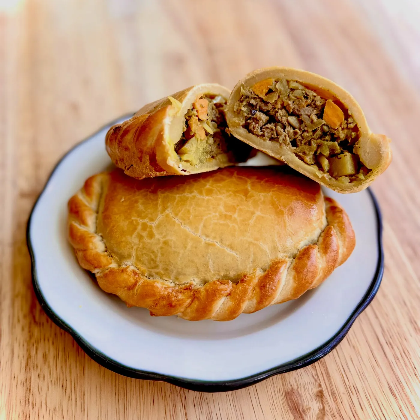 A crimped hand pie on a white plate, with a second pie broken open to show a beef and vegetable filling