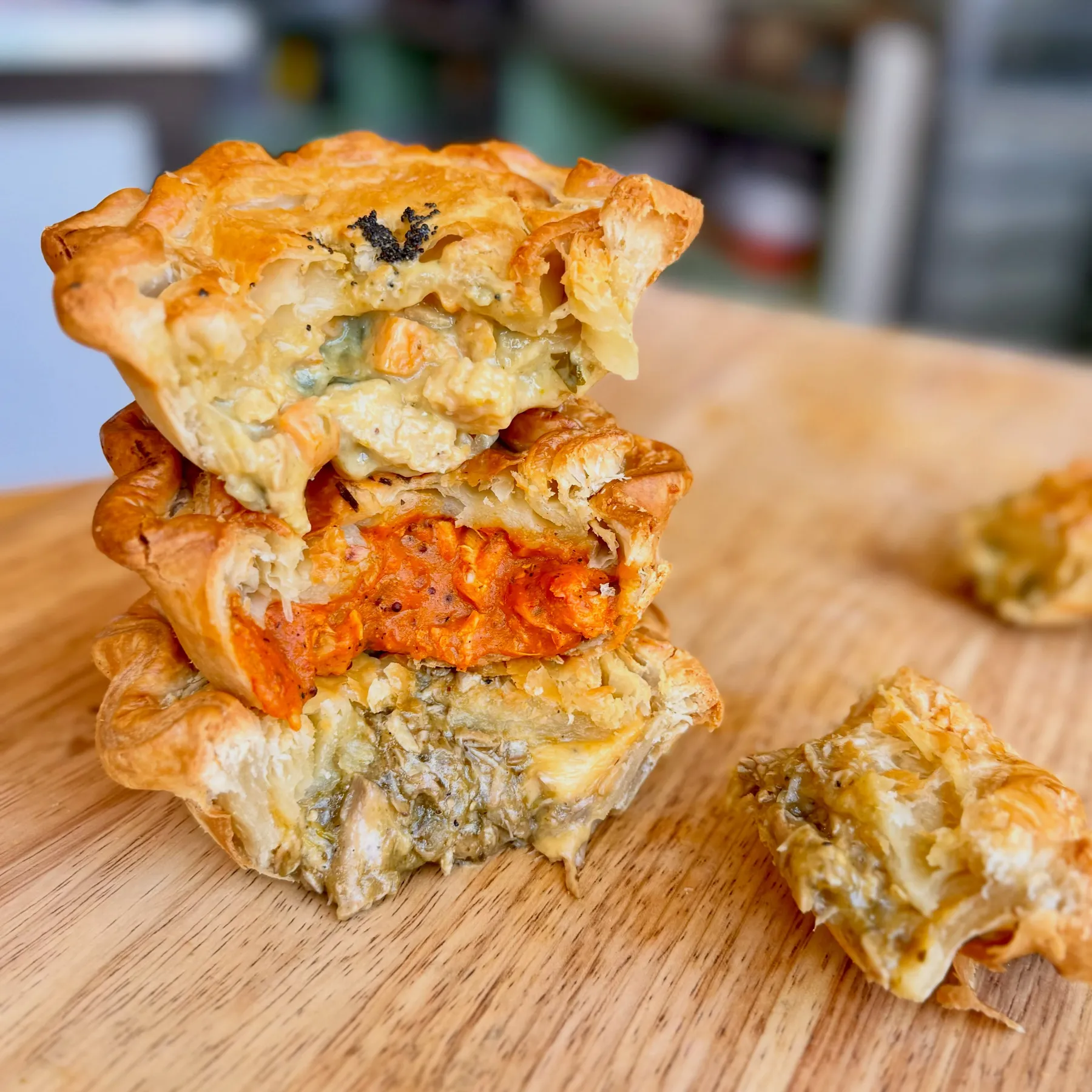 Three savory hand pies cut in half and stacked on a wooden board, showing flaky crust and fillings