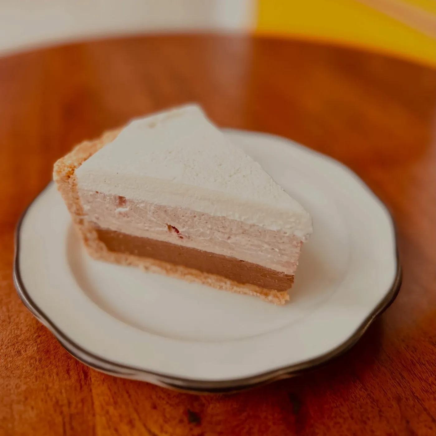 A tall slice of cream-topped pie on a white plate with a black rim