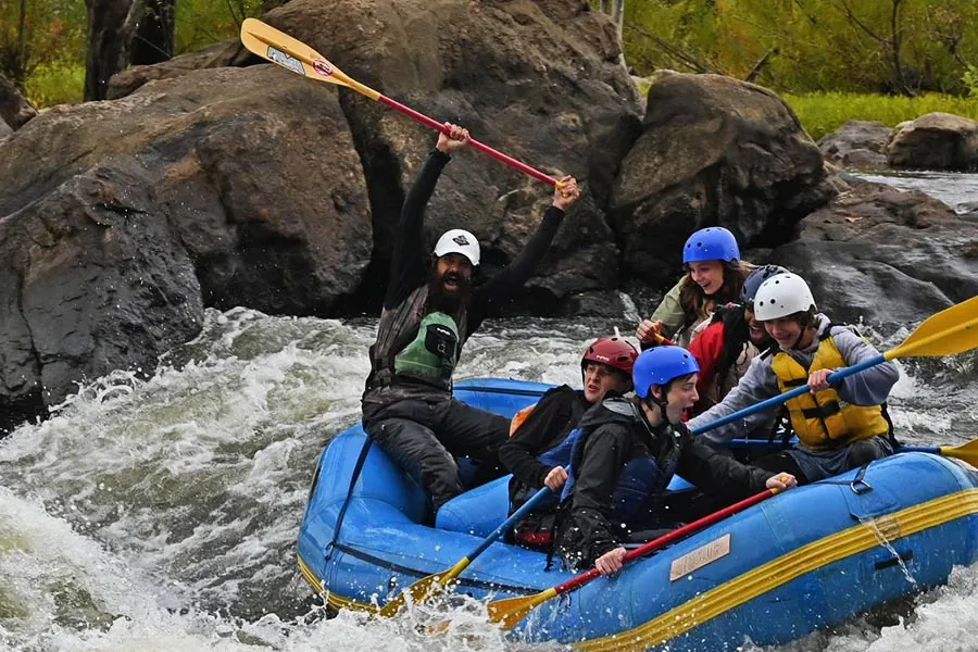 A Riverside raft crew with paddles in the air in front of big rocks and whitewater