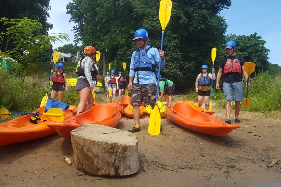 A group carrying orange kayaks down a sandy river trail