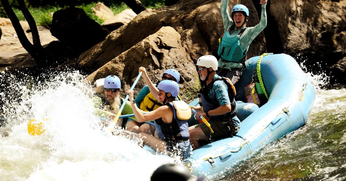 A Riverside Outfitters raft crew with paddles raised in whitewater