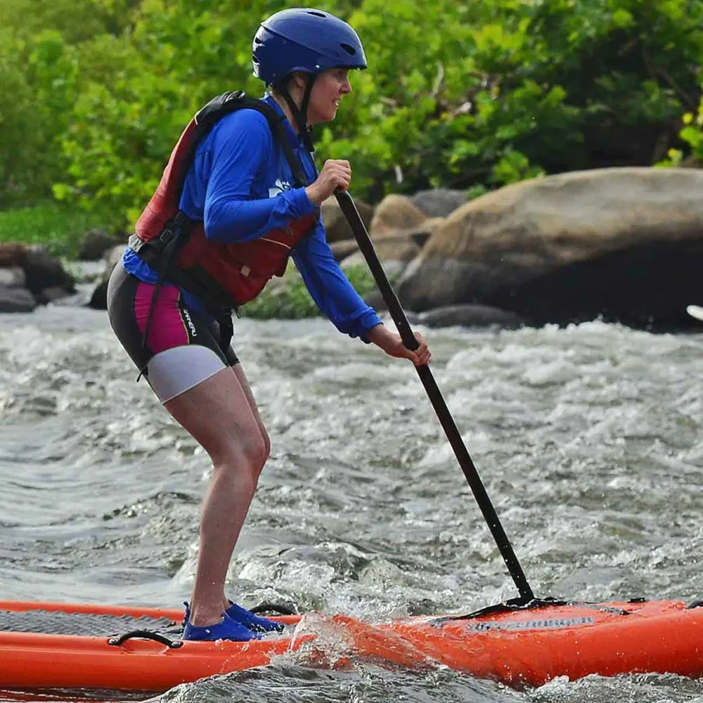 A paddler standing on an orange paddleboard in moving water