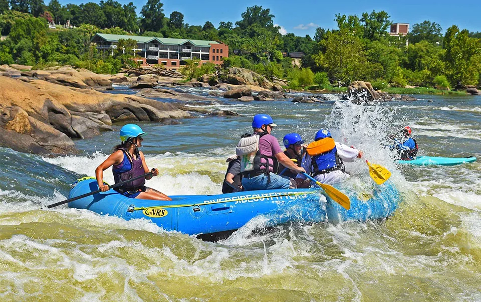 Rafters paddling hard through a rapid with downtown buildings behind them