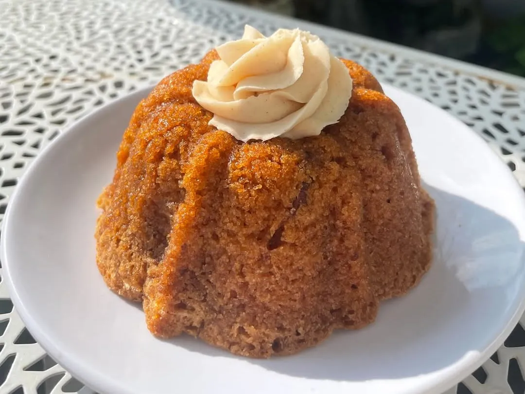 A small apple bundt cake with a swirl of frosting on a white plate outdoors
