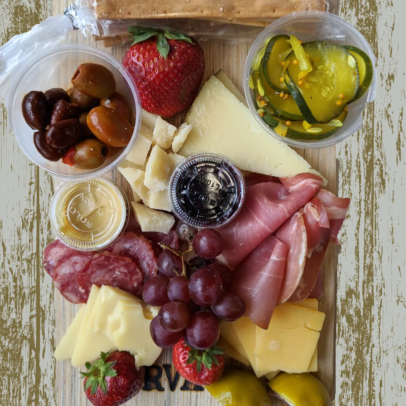 A charcuterie board with cured meats, cheeses, olives, strawberries, and grapes