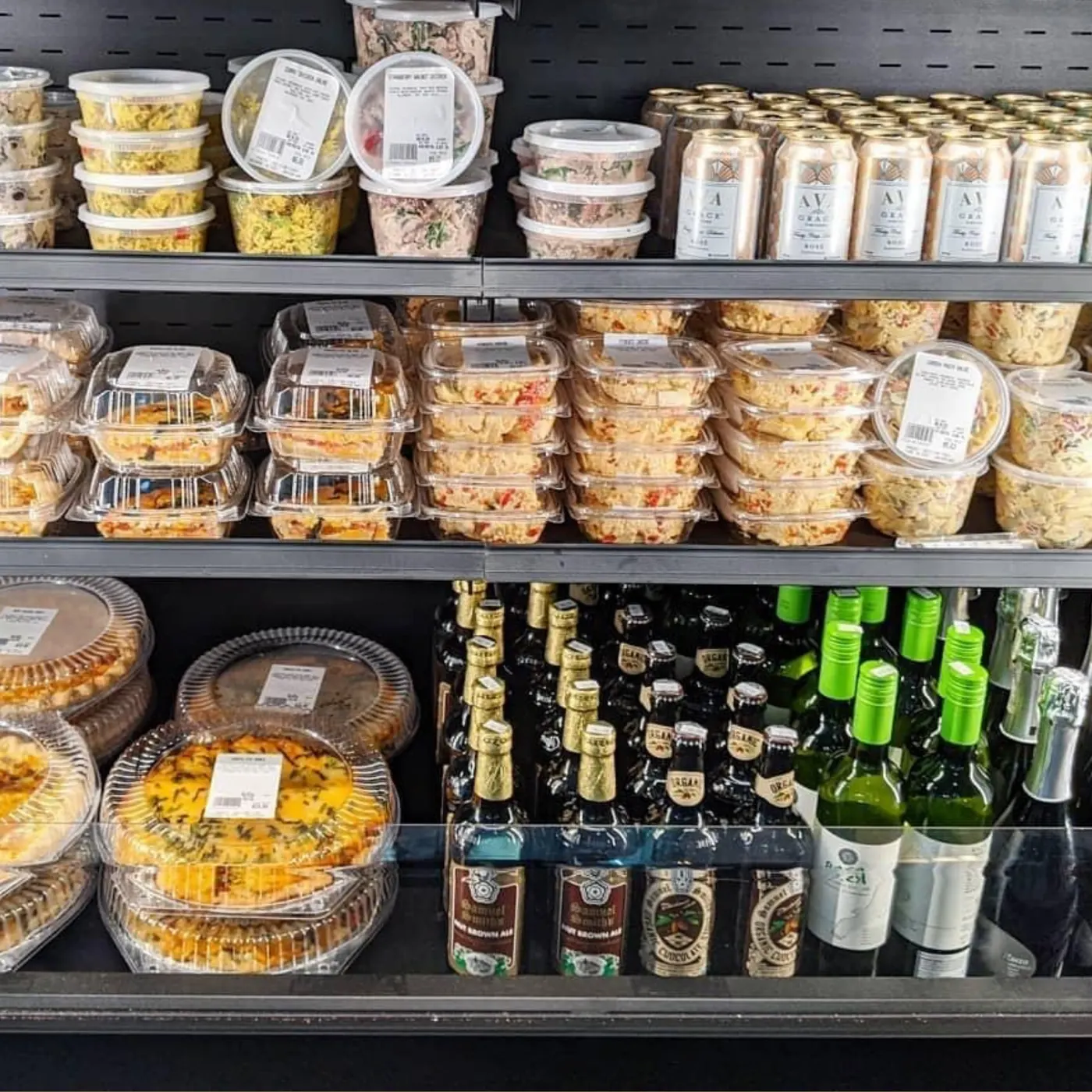 A refrigerator case of grab-and-go salads, dips, and quiche above a row of wine bottles