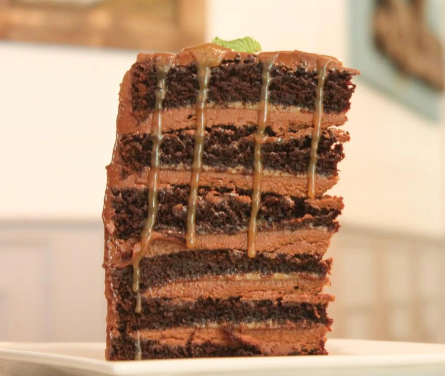 A tall slice of Salted Chocolate Caramel cake: dark chocolate layers and chocolate buttercream, with caramel dripping down the side