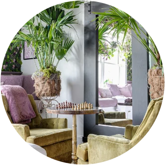 Green velvet armchairs around a chess table among tall palms